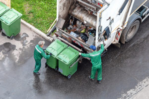 To menn som tømmer søppeldunker inn i søppelbilen.