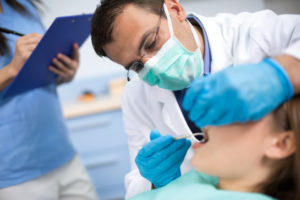 Tannlege med munnbind på undersøker pasientens tenner.